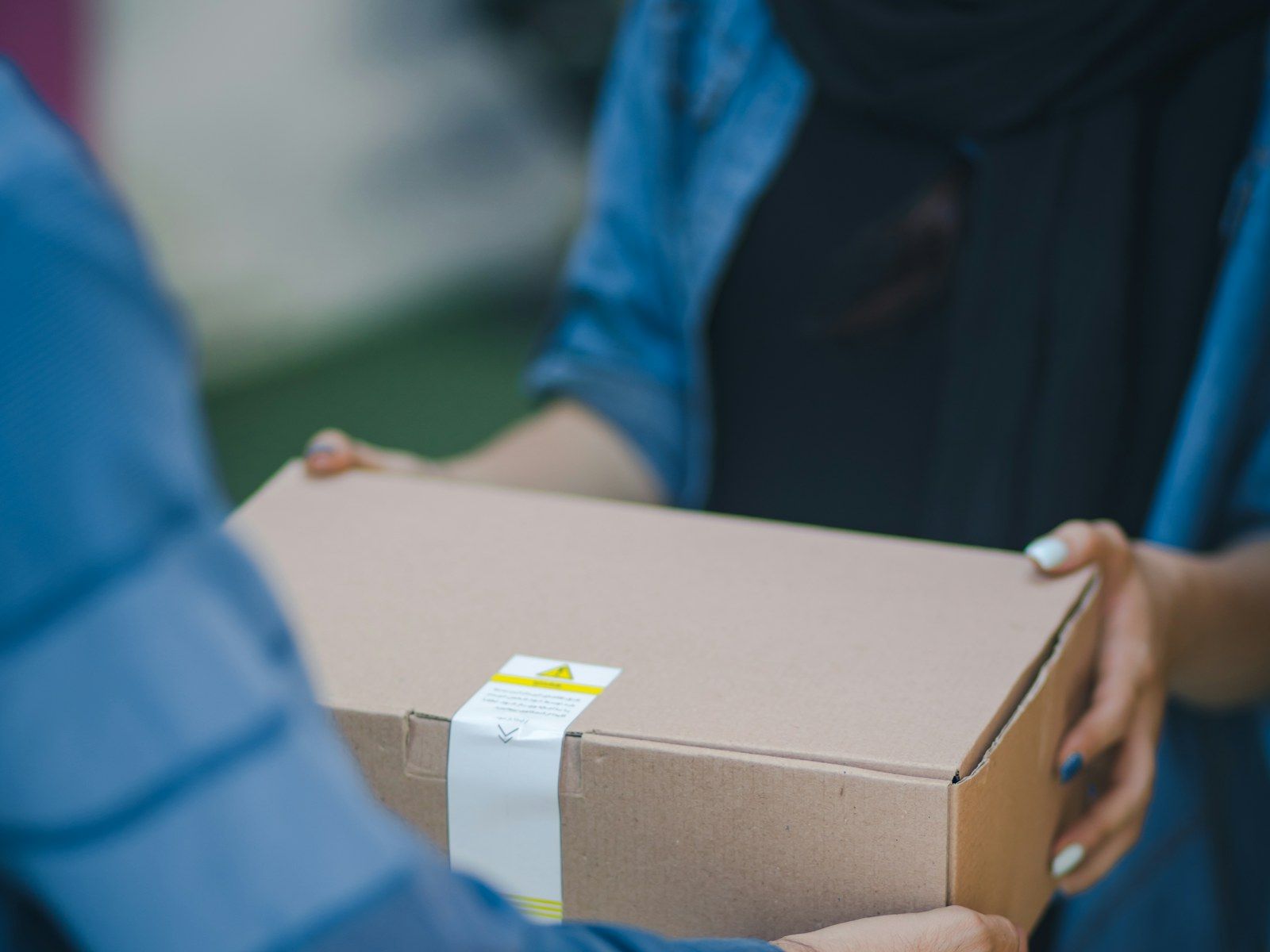 A 1Courier driver handing off a sealed cardboard parcel to a customer at the door